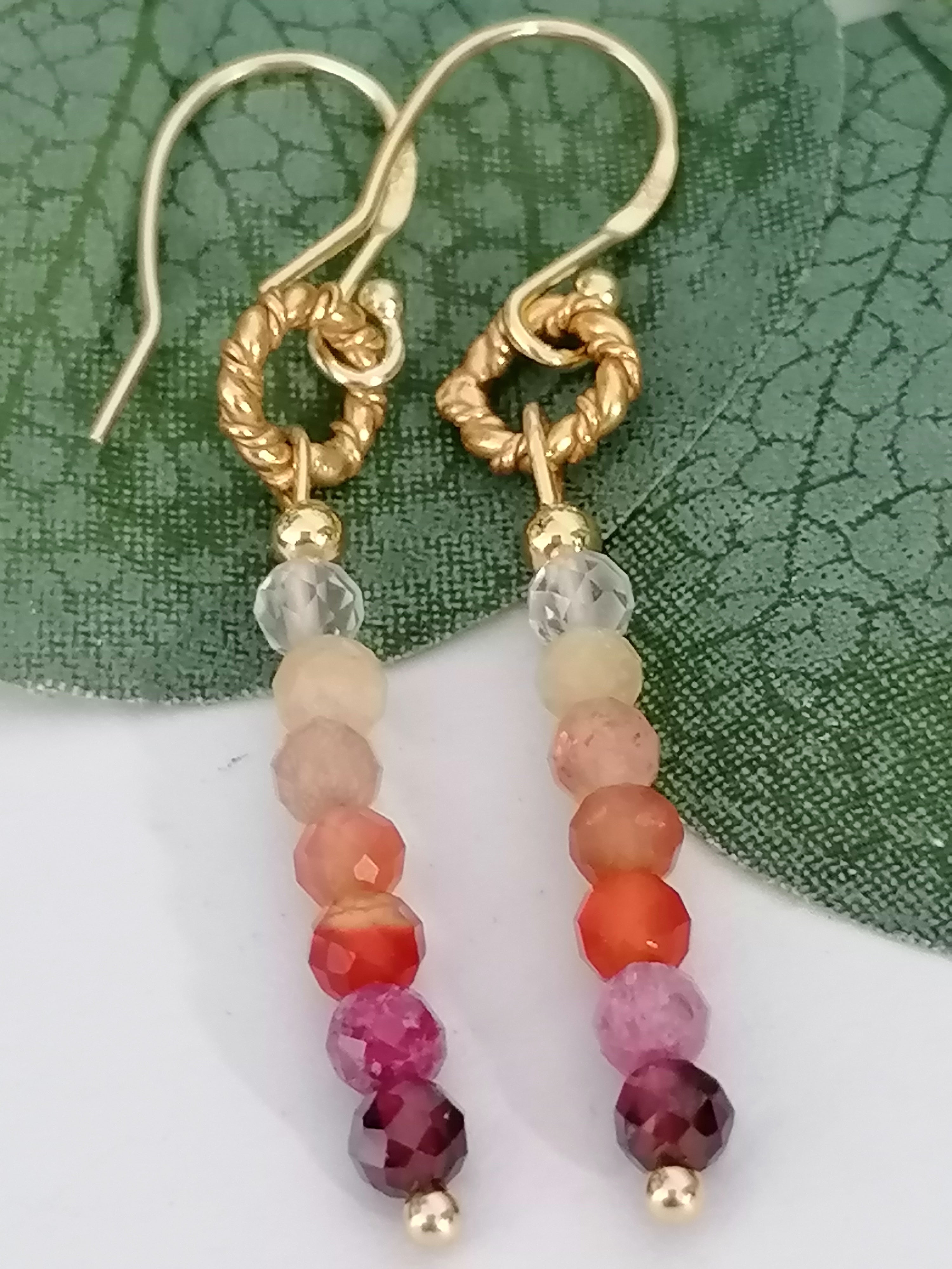 Gradient gemstone drop earrings with gold twisted ring hooks on a green leaf background