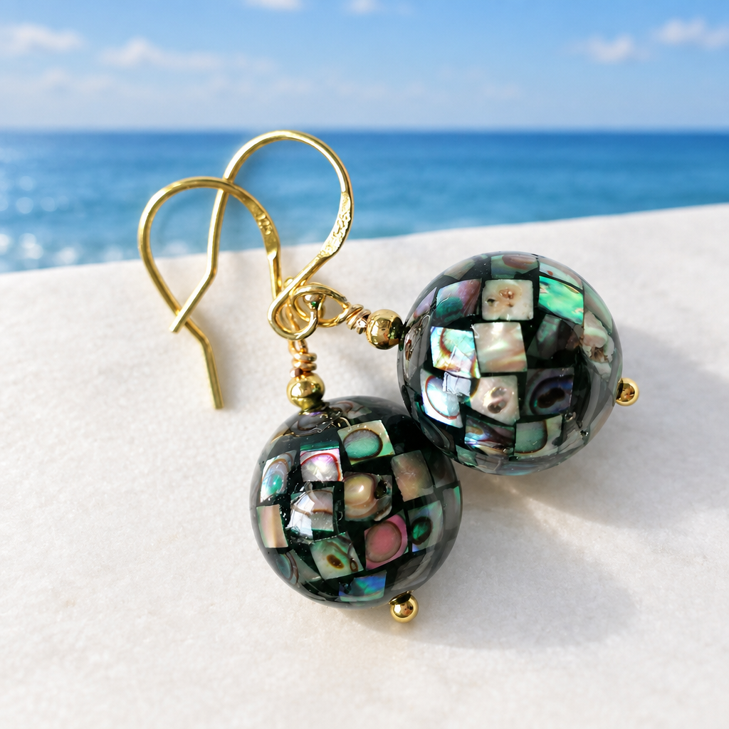 Abalone shell mosaic ball earrings on 24ct gold vermeil ear hooks, laid flat on a white surface with a coastal blue sky horizon