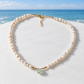 Cultured freshwater pearl and aquamarine teardrop necklace on a white surface by a blue coastal horizon
