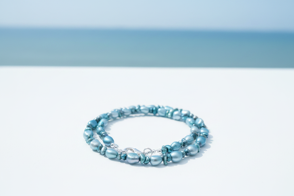 Blue and teal cultured freshwater pearl necklace with silver lobster clasp on coastal background