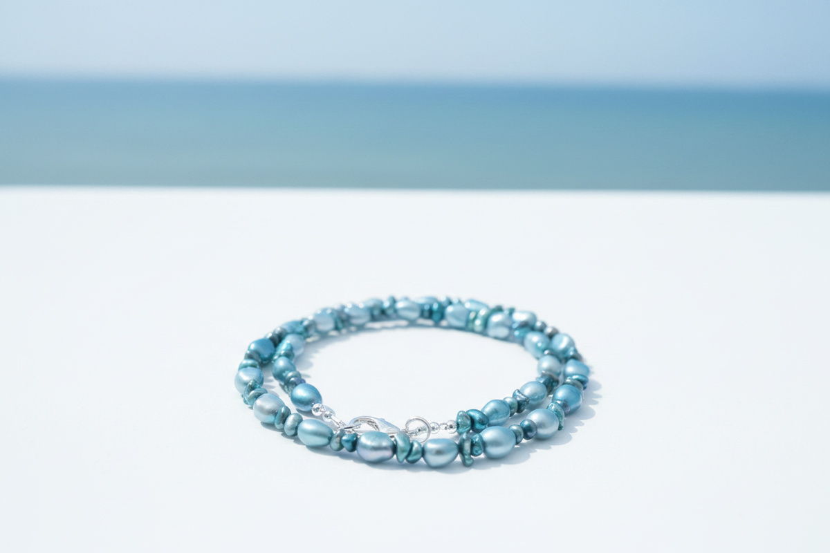 Blue and teal cultured freshwater pearl necklace with silver lobster clasp on coastal background