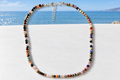 Dainty multicolour faceted gemstone bead necklace with silver lobster clasp and extender chain on a white surface with coastal sea view