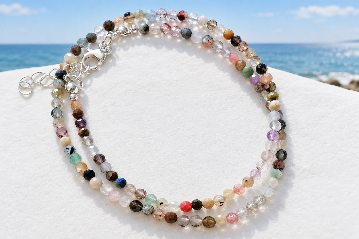 Dainty multicolour faceted gemstone bead necklace with silver lobster clasp and extender chain on a white surface with coastal sea view