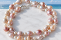 Pink and peach baroque freshwater pearl necklace with white seed pearls and silver clasp on a white surface with coastal sea view