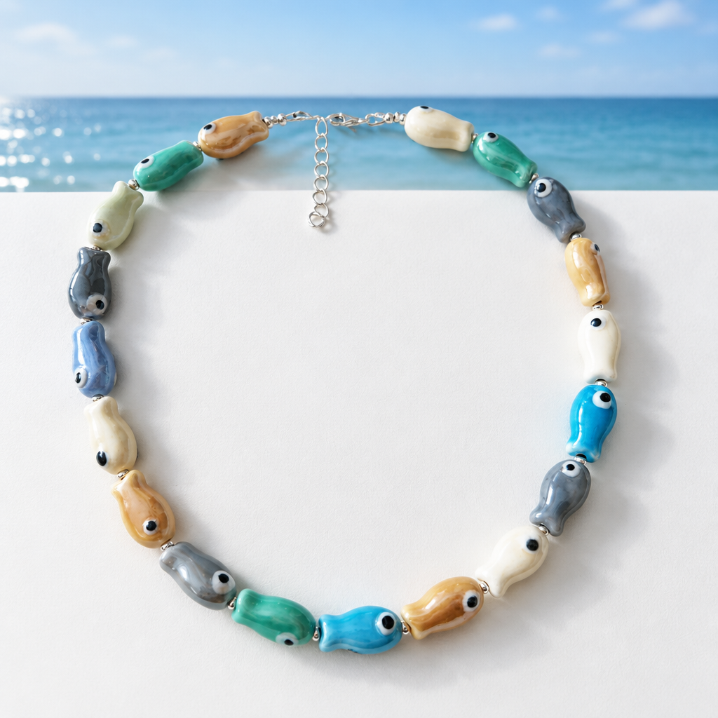 Ceramic fish necklace with silver clasp on white surface against a coastal blue horizon